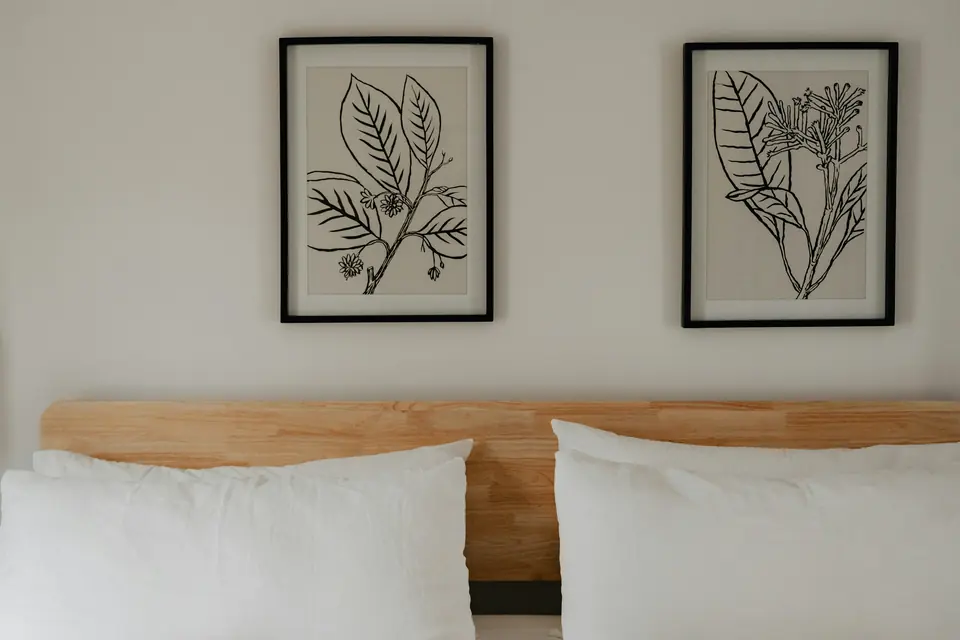Testiera in legno chiaro e stampe botaniche sopra il letto della Camera Bora
